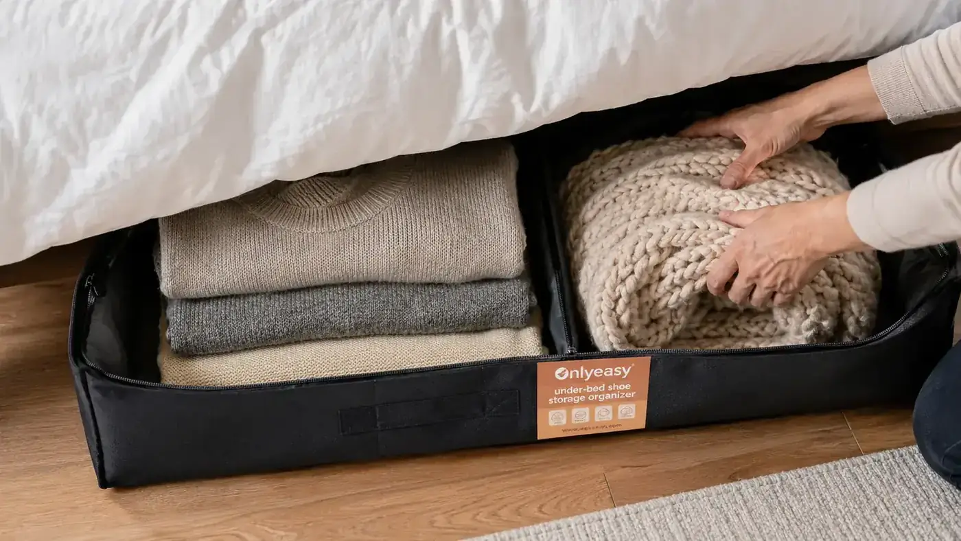 Folded out-of-season sweaters and a rolled blanket stored flat in an under-bed organizer tray