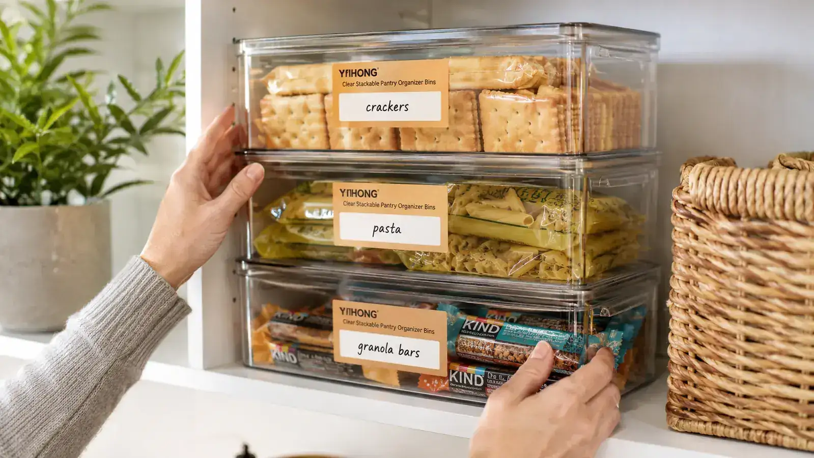 Clear pantry bins stacked neatly on a shelf with labels on the front, showing visible contents inside each bin
