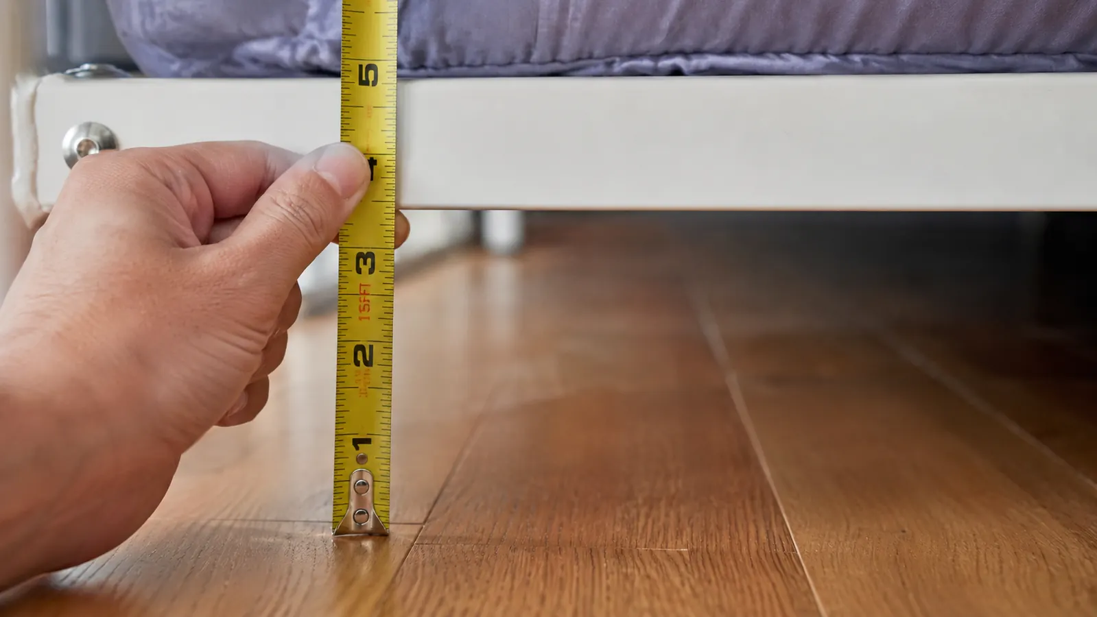 A ruler measuring the clearance gap between a bed frame and the floor, showing approximately four inches of height
