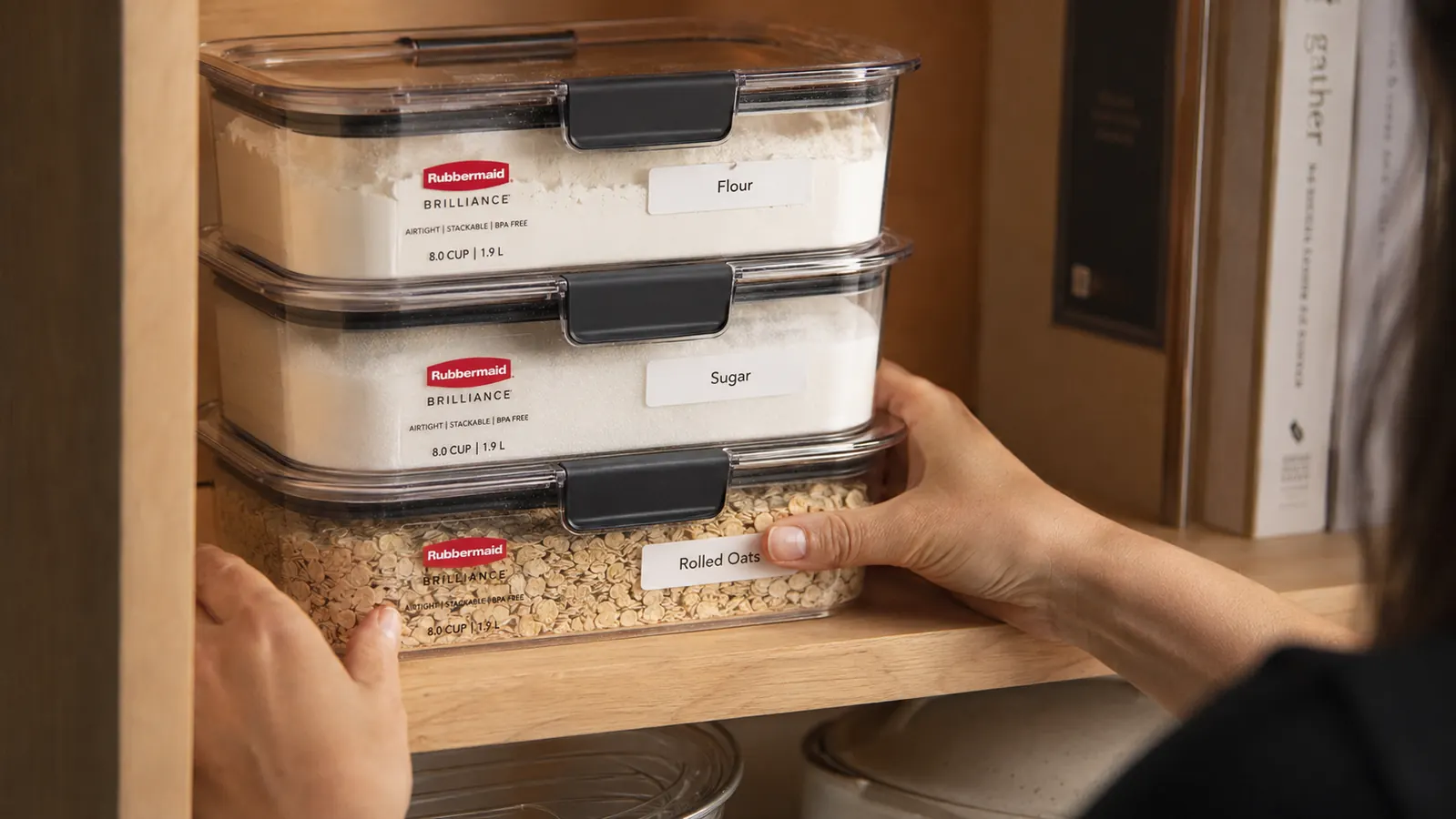 Labeled airtight containers stacked neatly on a pantry shelf with handwritten labels for flour, sugar, and oats
