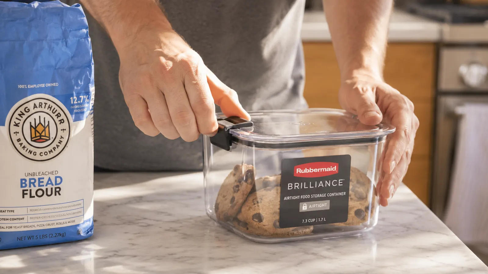 Hand pressing down the locking side tab on a Rubbermaid Brilliance container lid to seal it shut